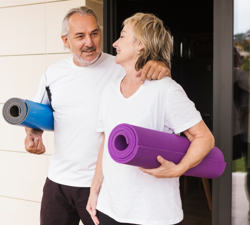 Un couple de seniors faisant du yoga dans un salon lumineux, symbolisant l’harmonie entre mouvement, respiration et bien-être au quotidien.