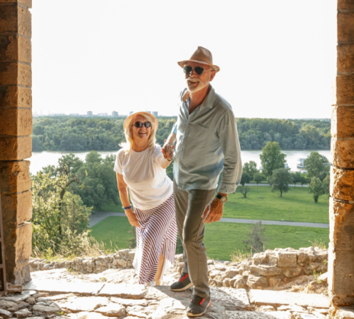 Couple senior souriant devant un jardin lumineux, illustrant la joie de vivre, la vitalité et l’équilibre prônés par la communauté Hermonie.
