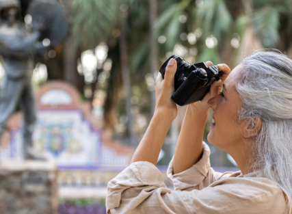 Femme de plus de 55 ans tenant un appareil photo en extérieur, souriante et détendue.